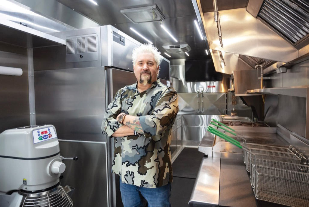 Guy Fieri in the kitchen with his arms crossed.